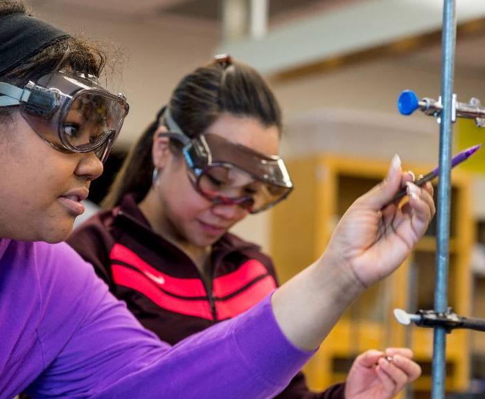 Two students wear goggles and examine a measuring instrument